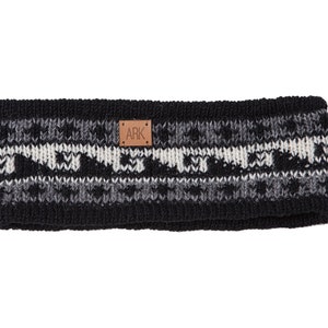 Könnte beinhalten: Ein schwarz-weiß-graues Strickstirnband mit geometrischem Muster. Das Stirnband hat ein kleines braunes Lederetikett mit den Buchstaben "ARK". Dieses Winteraccessoire soll die Ohren warm halten.