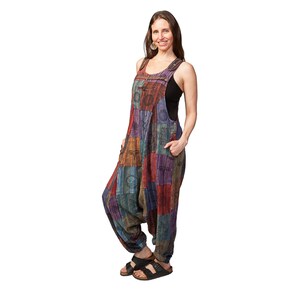 May include: A woman wearing a multi-coloured patchwork jumpsuit with a black tank top underneath. The jumpsuit has a loose, flowing fit and features a variety of patterns and designs.