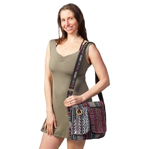 May include: A woman wearing a green sleeveless dress is holding a black and multi-colored patterned shoulder bag with a wooden ring accent. The bag has a long adjustable strap.