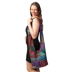 May include: A multi-coloured patchwork shoulder bag with a long strap. The bag features a variety of patterns and colours, including red, blue, green, and purple. It has a wooden button closure and a large capacity.