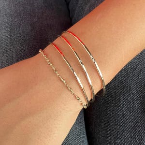 May include: Four gold bangles with a hammered texture and a delicate gold chain bracelet.