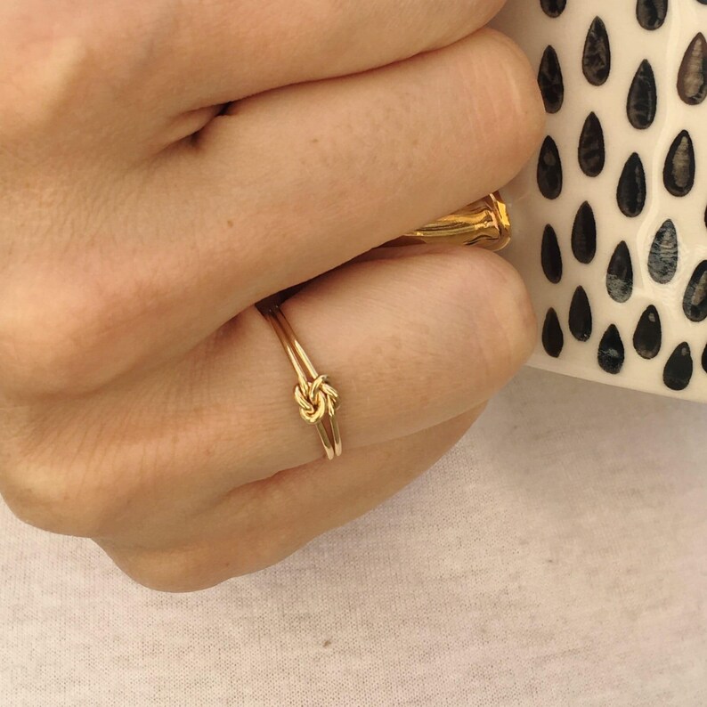 A close-up view of a person's hand wearing a gold ring with a knot design.