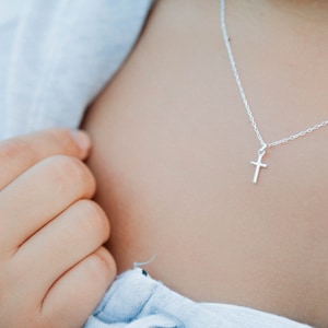 Puede incluir: Un collar de cadena de plata con un pequeño colgante de cruz de plata.