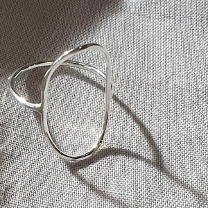 May include: A silver ring with a unique, open, oval design. The ring is made of a smooth, polished metal and has a simple, modern style.