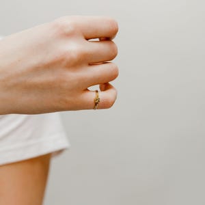 A close-up view of a person's hand wearing a gold Double Knot Ring with the ring visible on the ring finger.