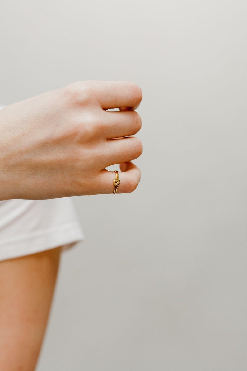 A close-up view of a person's hand wearing a gold Double Knot Ring with the ring visible on the ring finger.