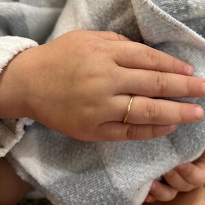 May include: A thin gold band ring on a finger.