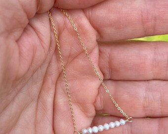 May include: A delicate gold chain necklace with a row of small white pearls. The necklace is simple and elegant, perfect for everyday wear.