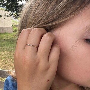 Op de afbeelding: Een dunne, goudkleurige ring wordt aan een vinger gedragen. De ring heeft een eenvoudig, elegant ontwerp met een glad, gepolijst oppervlak. De ring is een minimalistisch ontwerp, perfect voor dagelijks gebruik. De ring is een klassiek sieraad.