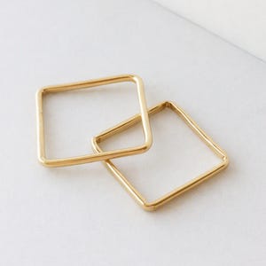 以下が含まれることがあります： 角が丸いゴールドトーンの金属製正方形フレーム2つ。フレームは薄く、中空で、滑らかで光沢のある仕上げが施されています。それらは互いに重なり合うように配置されており、きれいなラインと反射面を持つ幾何学的な構成を作り出しています。