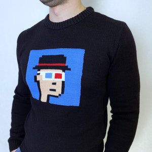 May include: Black knitted sweater with a blue square graphic of a pixelated person wearing a black hat and 3D glasses.