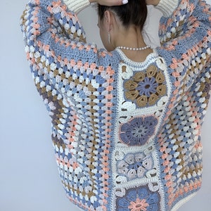 Puede incluir: Un cárdigan de ganchillo con un patrón de cuadrados de la abuela en tonos de azul, rosa, beige y marrón. El cárdigan tiene un corte holgado y mangas largas.