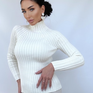 May include: A white ribbed turtleneck sweater with long sleeves. The sweater is fitted and has a slightly cropped length.