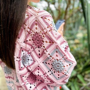 May include: A pink and grey crochet sweater with a square pattern. The sweater has a loose fit and is made with a soft yarn.