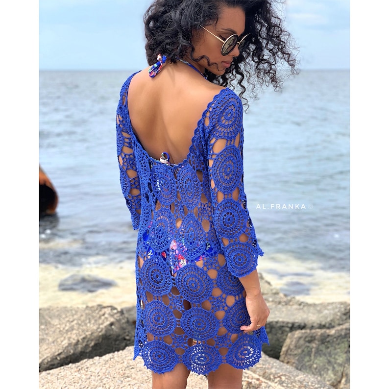 K&ouml;nnte beinhalten: Ein k&ouml;nigsblaues H&auml;kelkleid mit einem kreisf&ouml;rmigen Muster. Das Kleid hat einen tiefen V-Ausschnitt und 3/4 &Auml;rmel. Das Model tr&auml;gt das Kleid &uuml;ber einem Blumenbikini.
