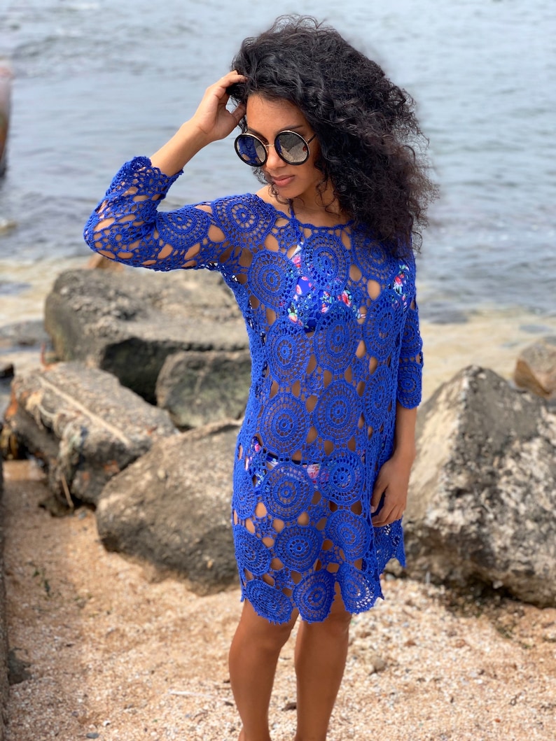 K&ouml;nnte beinhalten: Ein k&ouml;nigsblaues H&auml;kel-Strandkleid mit einem kreisf&ouml;rmigen Muster. Das Kleid hat lange &Auml;rmel und eine lockere Passform.