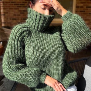 Peut inclure: Un pull en tricot épais vert forêt doté d'un col roulé montant, de manches longues avec poignets côtelés et d'une construction en fil texturé. Le vêtement présente une coupe décontractée avec un motif côtelé vertical sur tout le corps.