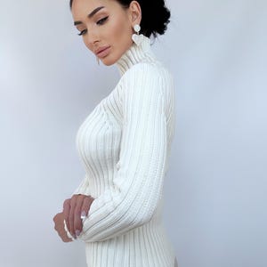 May include: A white ribbed turtleneck sweater with long sleeves. The sweater is fitted and has a high neckline.