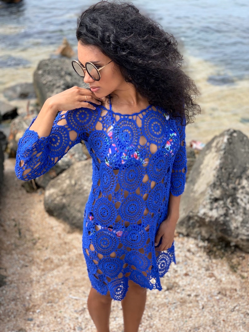 K&ouml;nnte beinhalten: Ein k&ouml;nigsblaues H&auml;kel-Strandkleid mit einem kreisf&ouml;rmigen Muster. Das Kleid hat lange &Auml;rmel und eine lockere Passform.