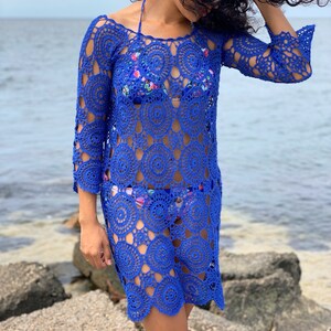 K&ouml;nnte beinhalten: Ein k&ouml;nigsblaues H&auml;kel-Strandkleid mit einem kreisf&ouml;rmigen Muster. Das Kleid hat lange &Auml;rmel und eine lockere Passform.