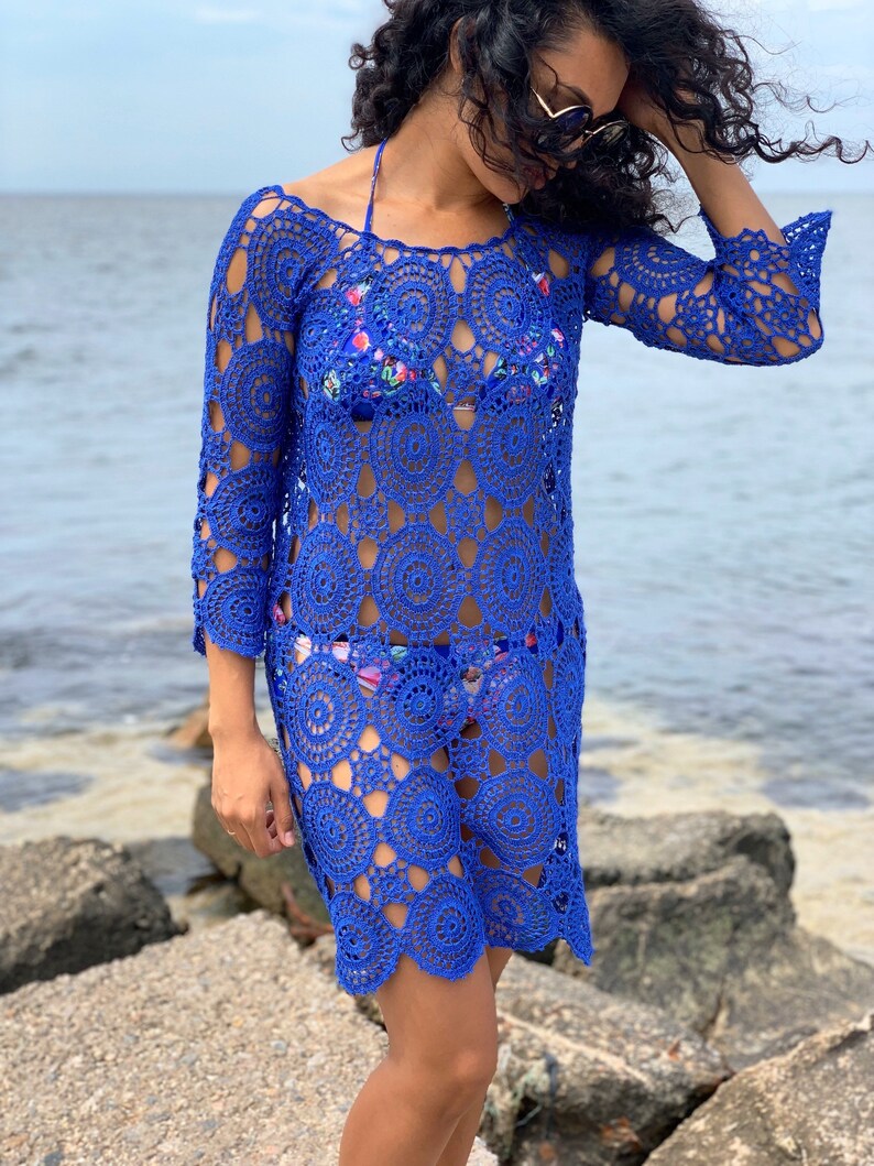 K&ouml;nnte beinhalten: Ein k&ouml;nigsblaues H&auml;kel-Strandkleid mit einem kreisf&ouml;rmigen Muster. Das Kleid hat lange &Auml;rmel und eine lockere Passform.