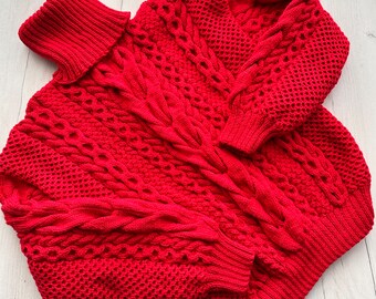 May include: A vibrant red knitted sweater with a turtleneck and intricate cable and openwork patterns. The sweater features long sleeves with ribbed cuffs and a relaxed fit, perfect for cozy wear.
