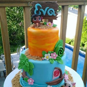 Puede incluir: Tarta de dos pisos con glaseado azul y naranja, decorada con un personaje de dibujos animados, flores y un letrero de madera que dice "Eva". La tarta tiene una base arenosa y una peque&ntilde;a figura de cerdo. El texto "pie's cake shop" est&aacute; en la parte inferior.