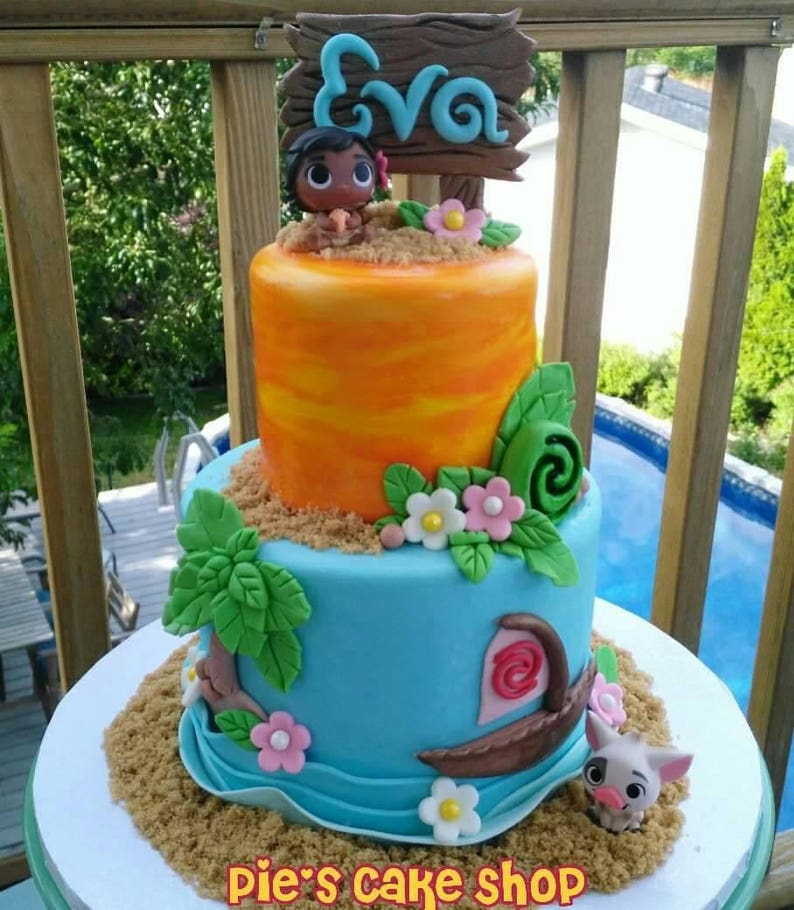 Puede incluir: Tarta de dos pisos con glaseado azul y naranja, decorada con un personaje de dibujos animados, flores y un letrero de madera que dice "Eva". La tarta tiene una base arenosa y una peque&ntilde;a figura de cerdo. El texto "pie's cake shop" est&aacute; en la parte inferior.