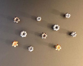Op de afbeelding: Een verzameling van tien zilveren en goudkleurige patroonhulzen, elk met een stervormig ontwerp. De hulzen zijn in een halve cirkel op een grijs oppervlak gerangschikt.