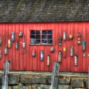 May include: A red wooden building with a window and a variety of colorful buoys hanging on the exterior. The buoys are made of wood and painted in various colors, including red, blue, green, yellow, and white.