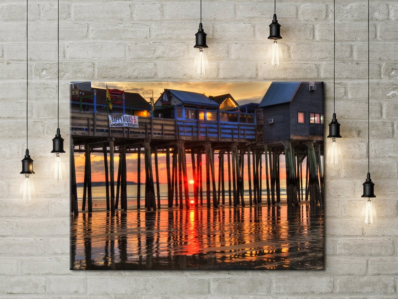 Pu&ograve; includere: Un ristorante colorato sul lungomare su palafitte sull'oceano al tramonto. Il ristorante ha un esterno blu e bianco con un cartello rosso che recita "Happy Hours 5-7". L'acqua riflette le tonalit&agrave; arancioni e rosa del tramonto.