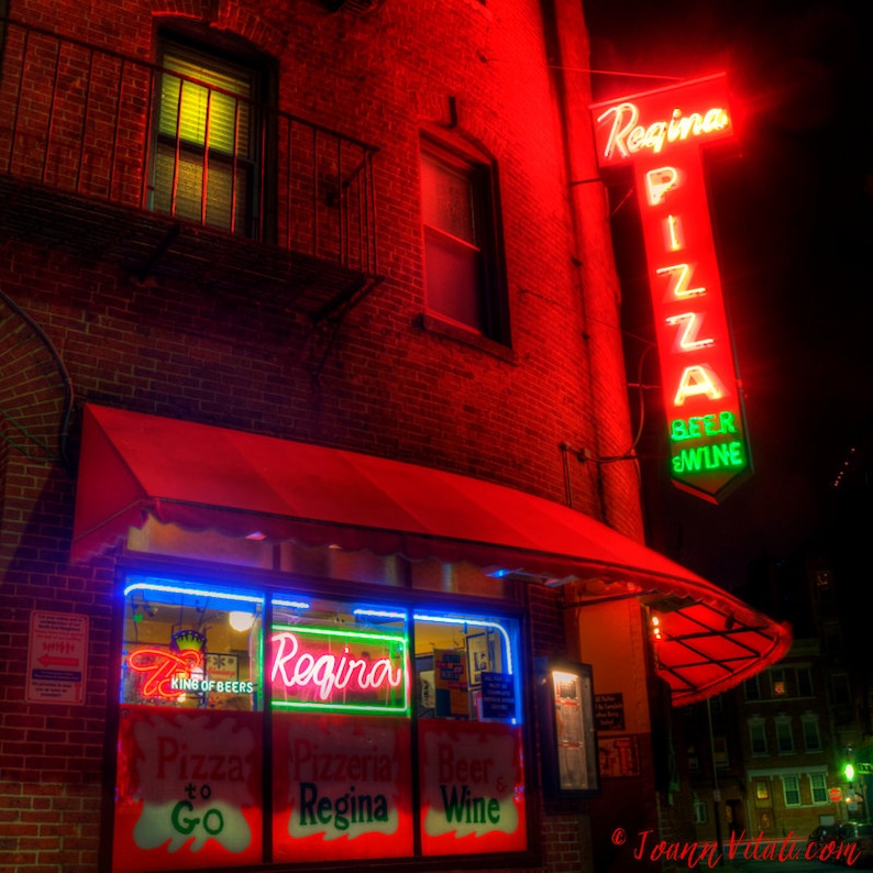 May include: A red brick building with a neon sign that reads "Regina Pizza Beer & Wine". The building has a red awning and a window with a neon sign that reads "Regina" and "Pizza to Go".
