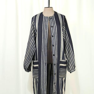 May include: A long, button-down duster coat with vertical stripes in navy blue and light grey. The coat has long sleeves, two front pockets, and is displayed on a mannequin. The fabric appears to be a lightweight material.
