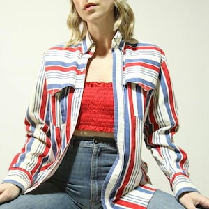 Könnte beinhalten: Ein Hemd mit roten, weißen und blauen vertikalen Streifen. Das Hemd hat zwei Brusttaschen und wird über einem roten Tube-Top getragen. Die Person trägt eine blaue Jeans.