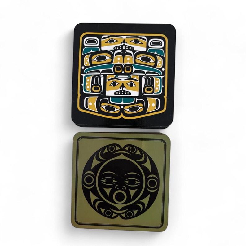 Puede incluir: Dos posavasos cuadrados con dise&ntilde;os de inspiraci&oacute;n nativa americana. Uno es negro con un dise&ntilde;o amarillo, verde azulado y blanco. El otro es verde oliva con un dise&ntilde;o de cara de sol negra. Ambos son cuadrados y brillantes.