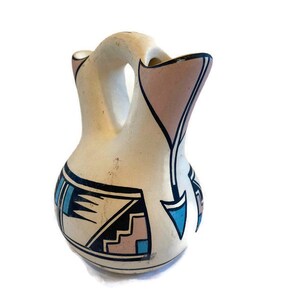 May include: A white ceramic pitcher with a geometric design in black, pink, and blue. The pitcher has two spouts and a handle.