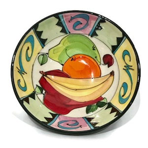 May include: A ceramic bowl with a colorful design featuring a banana, orange, pear, and apple. The bowl has a black rim and a white background with a geometric pattern.