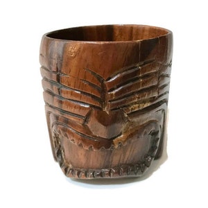 Può includere: Un mug tiki in legno con un design a faccia intagliata. Il mug è marrone e ha una finitura liscia e lucida.