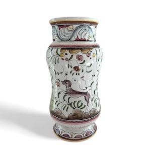 Peut inclure: Un vase en céramique blanc avec un motif peint à la main. Le vase présente un chien marron, des fleurs et des vignes. Le bord supérieur a un motif décoratif avec des accents bleus, jaunes et roses. La base a un design similaire. Le vase mesure environ 25 cm de haut.