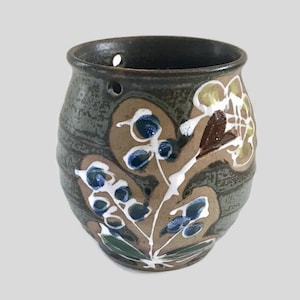 May include: A small, brown ceramic planter with a green glaze and white, blue and yellow floral designs. The planter has drainage holes in the bottom.