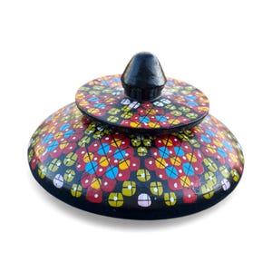 May include: A hand-painted, decorative wooden trinket box with a lid. The box and lid are black with a colorful floral pattern in red, yellow, blue, and white. The lid has a black knob.
