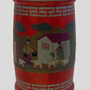 May include: Red cylindrical wooden container with a painted scene of people and animals in a rural setting. The container has a decorative border around the top and bottom.
