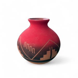 May include: A red ceramic vase with a rounded body and a narrow neck. The vase has a geometric design in black and tan, featuring a mountain-like pattern. The vase is likely handmade and has a rustic, Southwestern aesthetic.