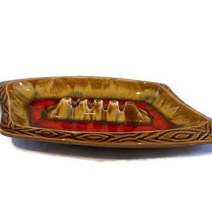 May include: A brown and red ceramic ashtray with a geometric design. The ashtray has four indentations for cigarettes.