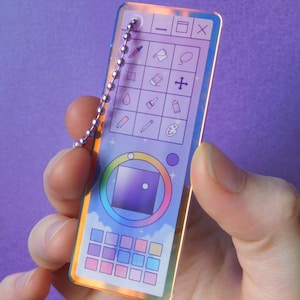 May include: A rectangular acrylic keychain with an iridescent finish featuring a digital art software interface design. The graphic includes a toolbar with icons, a color wheel, and a grid of color swatches, all attached to a silver ball chain.