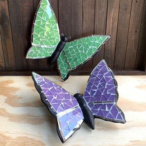 May include: Two mosaic butterfly wall decor pieces. One butterfly is green and the other is purple.