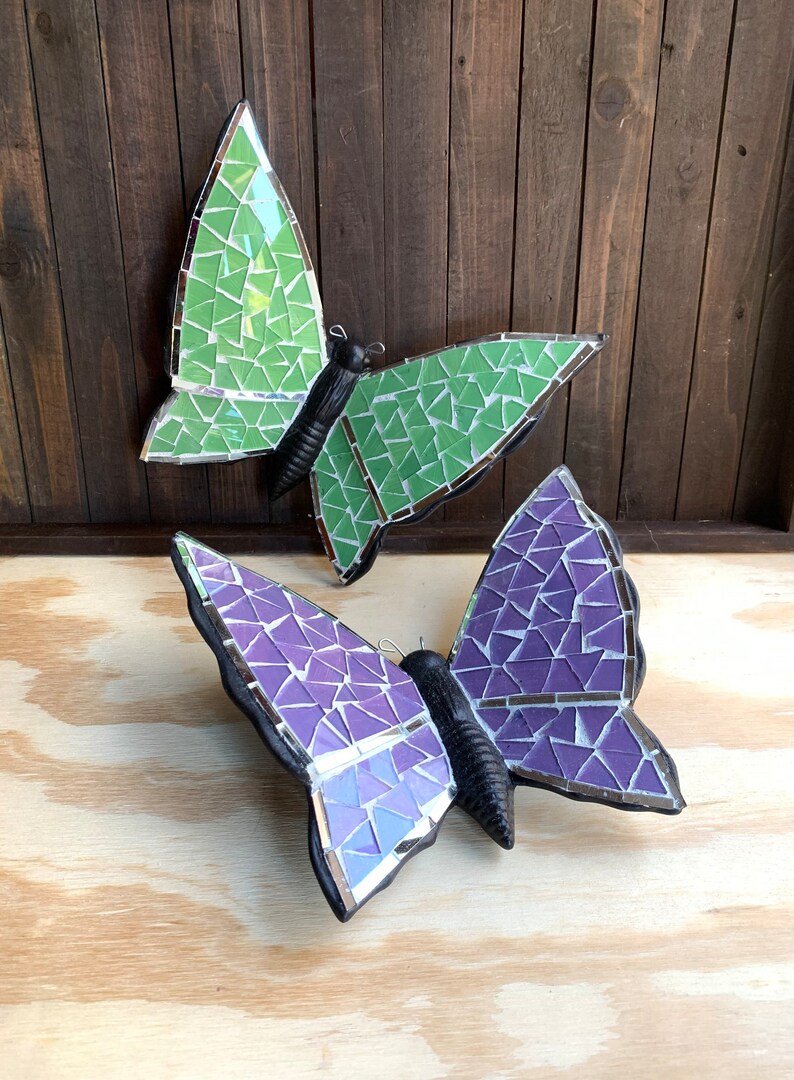 May include: Two mosaic butterfly wall decor pieces. One butterfly is green and the other is purple.