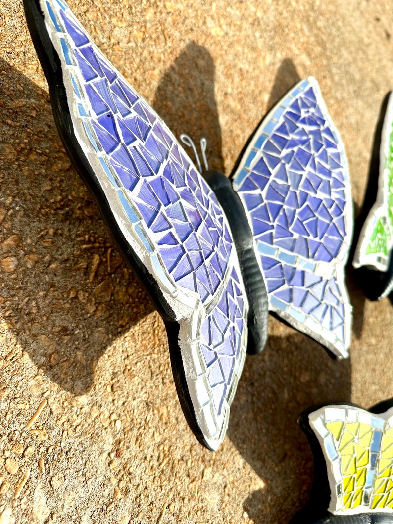 May include: A purple mosaic butterfly with black accents and silver detailing. The butterfly is made of small, iridescent tiles and has a textured surface.