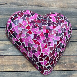 May include: A pink and purple mosaic heart-shaped wall decor. The heart is made of small, irregular pieces of glass that are arranged in a random pattern.