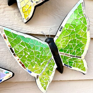 May include: A green mosaic butterfly with black wings and silver accents. The butterfly is made of small, iridescent glass tiles.